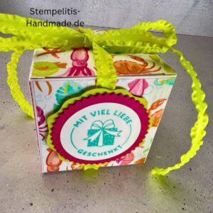 Handdekorierte Geschenkschachtel mit Schleife von oben, Geschenkschachtel mit liebevollem Aufkleber “Mit viel Liebe verschenkt”, Detailansicht Schleife auf Geschenkschachtel, Seitenansicht Geschenkschachtel mit buntem Designpapier, Offene Geschenkbox zum Befüllen, Geschenkschachtel auf hellem Hintergrund mit Dekorband, Handgemachte Geschenkverpackung mit grünem Band und Etikett